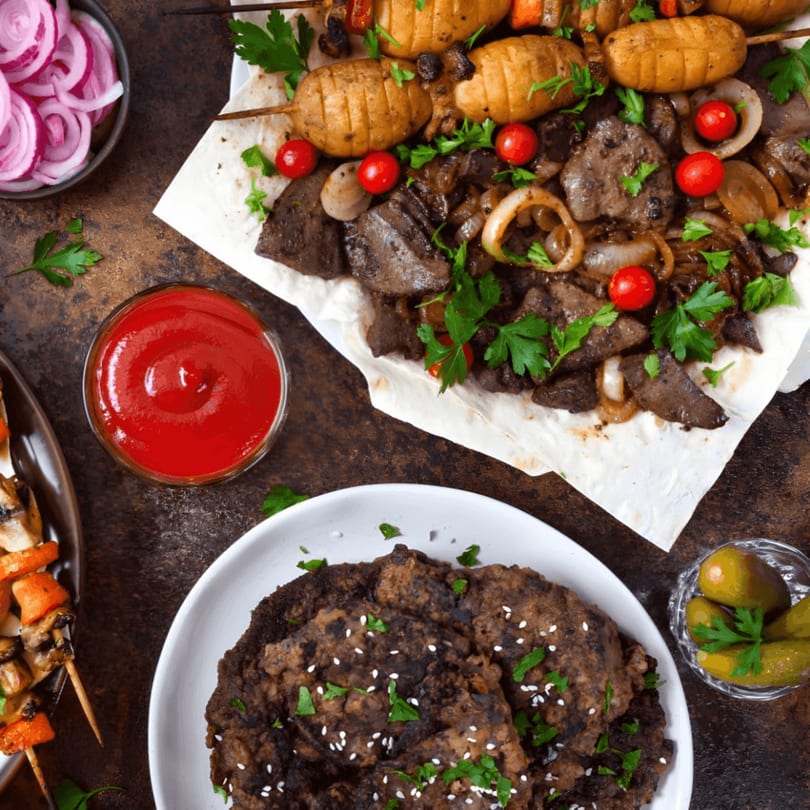 Mediterranean meal with grilled liver, onions, cherry tomatoes, potato skewers, and falafel with pickles.