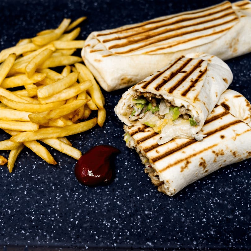 Two grilled Mediterranean wraps, one cut open, with a side of golden fries and a dollop of ketchup.